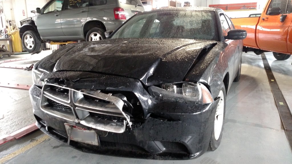 A black Dodge Charger with front-end collision damage on the shop floor